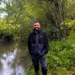 Will Procter, the GIS Analyst at South East Rivers Trust standing in front of a river.